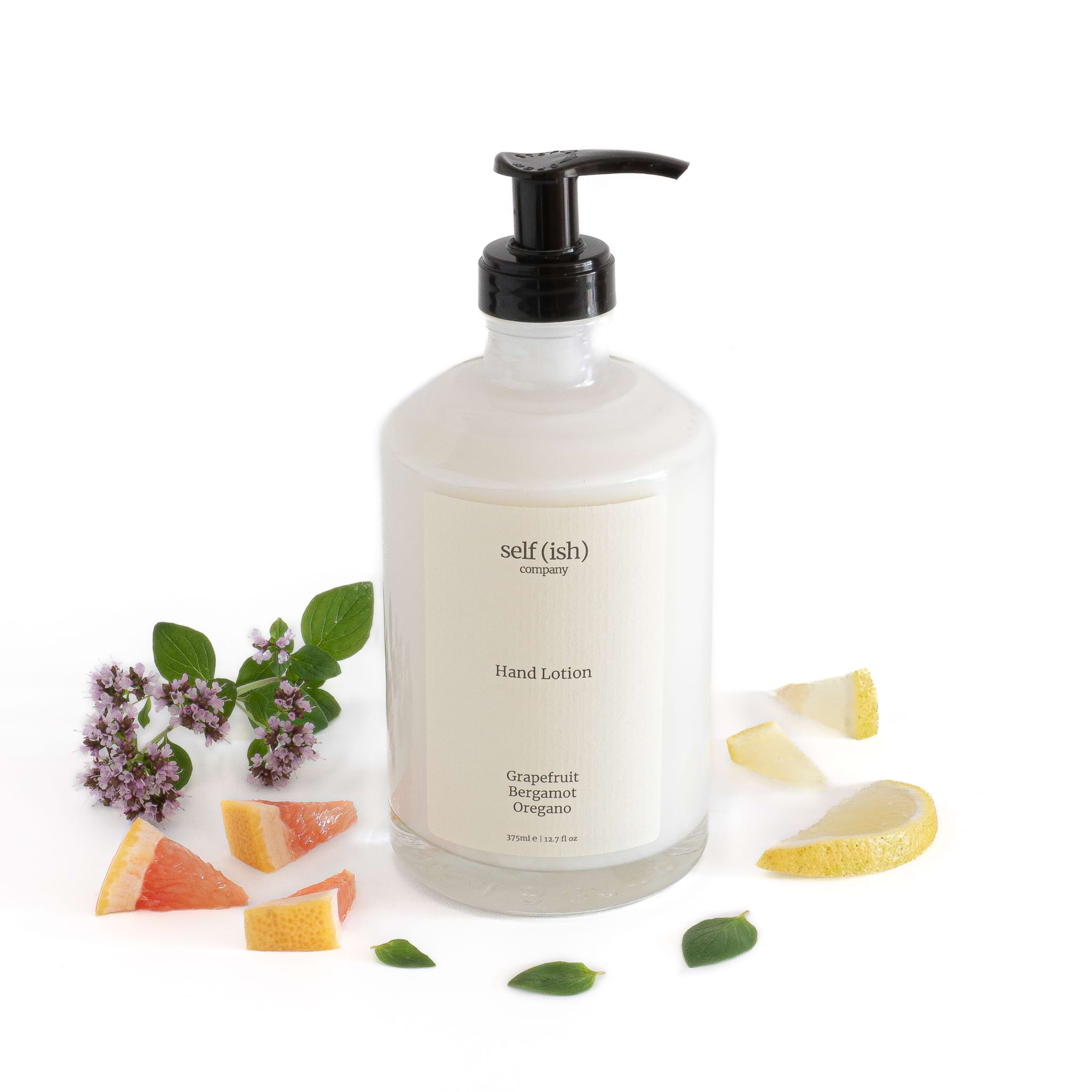 grapefruit hand lotion in luxury glass bottle surrounded by fresh grapfefruit oregano and bergamot 