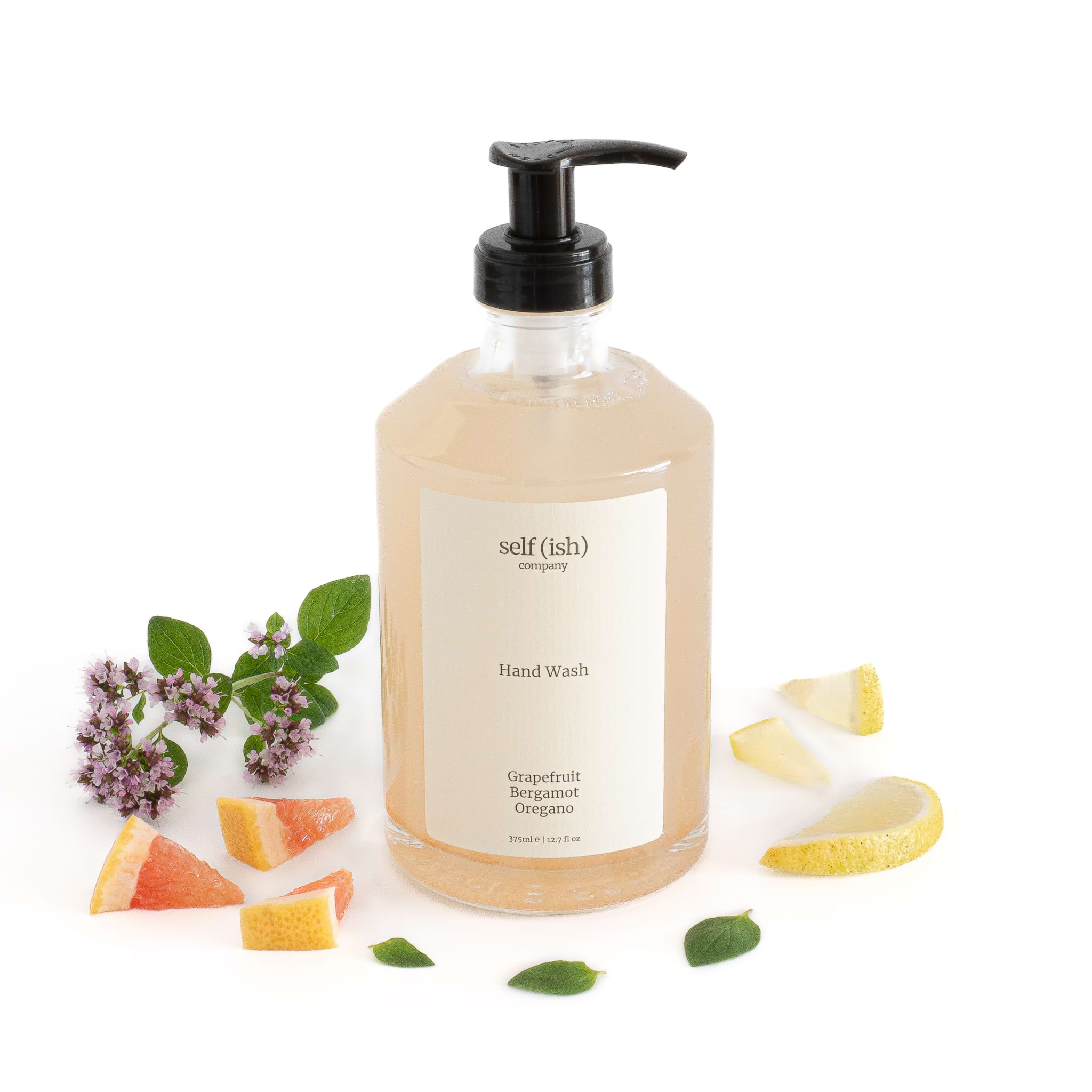 grapefruit hand wash in luxury glass bottle surrounded by fresh grapfefruit oregano and bergamot 